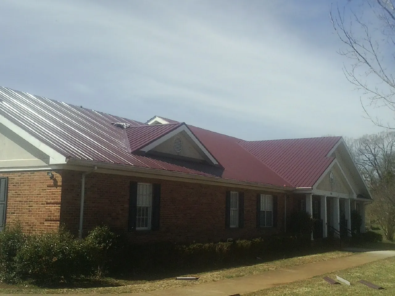 Red metal roof with gabled entries on a long brick building, from a Hail Damage Roof Repair job in Tarawa Terrace