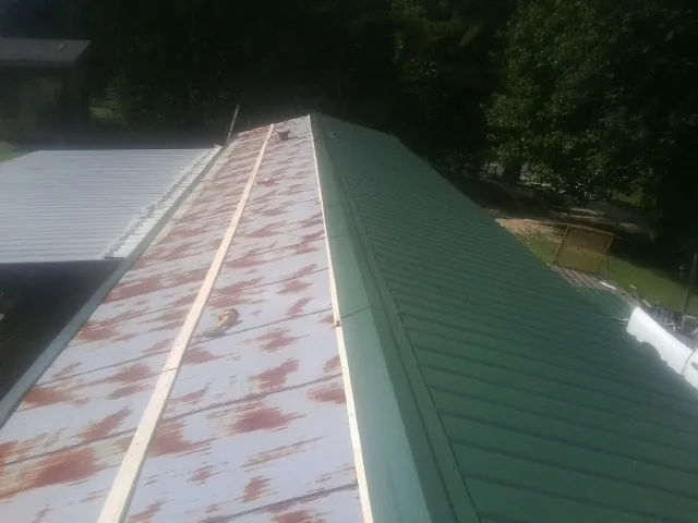 Old rusted panels beside newly installed green metal roofing — Wind Damage Roof Repair by Roofing Brothers in Tarawa Terrace
