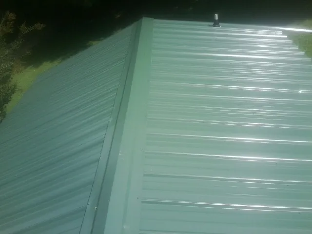 New green metal panels meeting at the ridge of a roof — Flat Roof Repair work by our crew in Tarawa Terrace