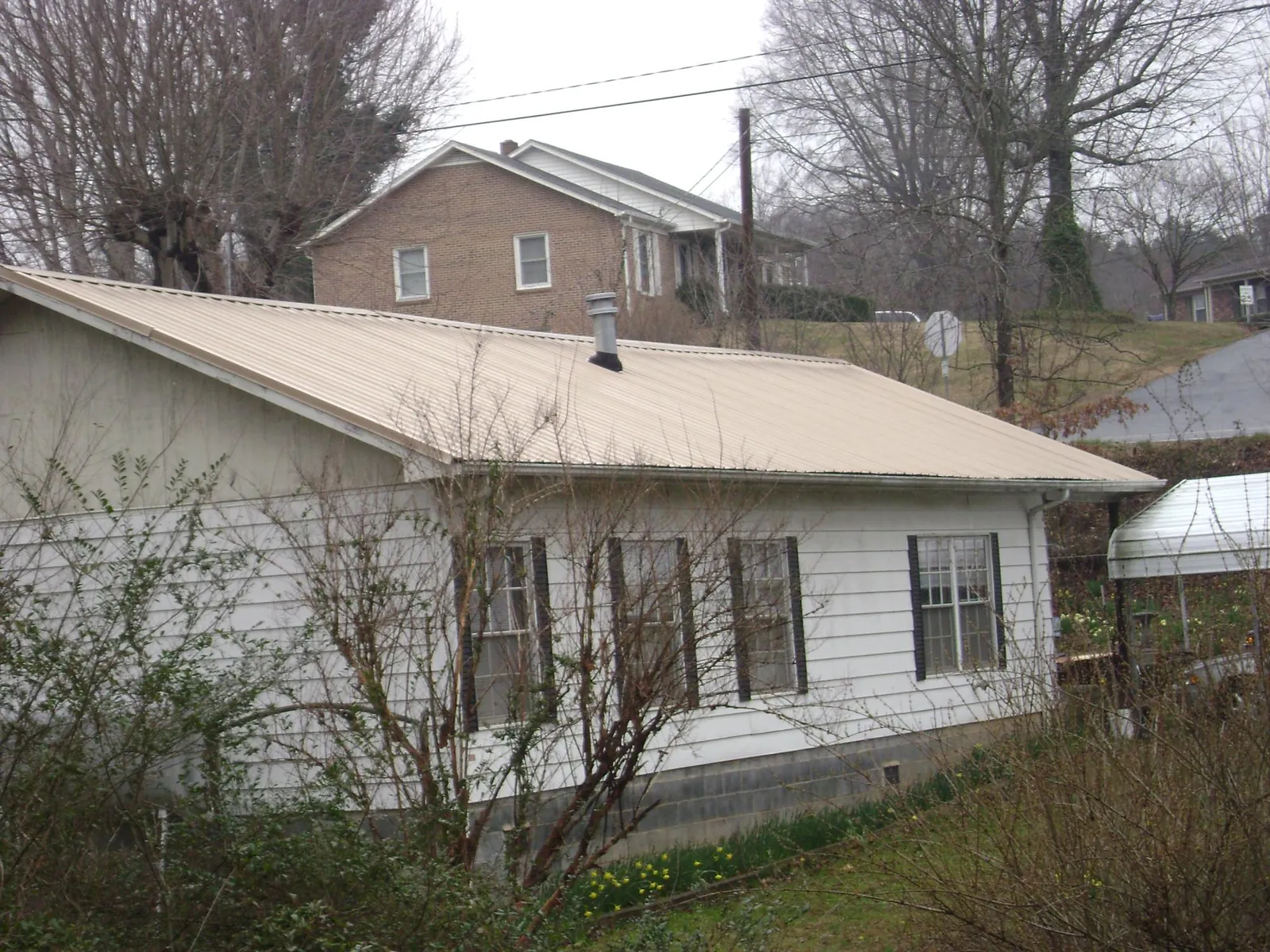 Tan metal roof on a white sided house set into a hillside — Commercial Roofing by Roofing Brothers in Tarawa Terrace